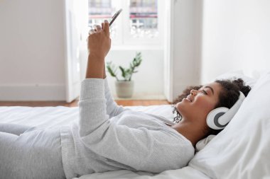 İspanyol kadın bir yatağa uzanıyor, kulaklık takıyor ve müzik dinliyor. Kulaklıkla çalan sese dalmış ve rahatlamış görünüyor..