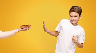 A young boy with a disgusted expression declining a hotdog from an outstretched hand. clipart