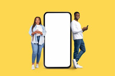 A smiling African American young man and woman flanking a large smartphone mockup on yellow studio background clipart