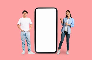 Mutlu Asyalı çift dev bir akıllı telefonun yanında poz veriyor. Pembe arka planda uygulama sunumları için ideal.