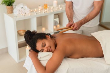 A spa therapist utilizes singing bowls for a sound therapy session with a peaceful African American lady, enhancing the holistic experience for people clipart