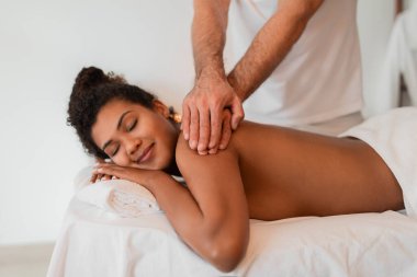 Siyahi bir bayanın barışçıl bir sırt masajı yaşadığı bir spa sahnesi. Terapistlerin elleri ve rahatlatıcı bir spa ortamı tarafından vurgulandı.