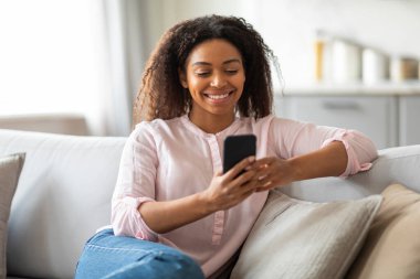 Ev ortamında cep telefonu kullanan siyahi bir kadın çağdaş çağdaş yaşam tarzı ve iletişim kuruyor.