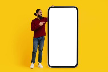 Sakallı Hintli adam neşeli bir şekilde dev, boş bir akıllı telefon ekranını işaret ediyor.