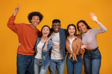 Çeşitli bir grup coşkuyla poz veriyor, çok ırklı, çok ırklı bir bağı paylaşıyor, turuncu bir zemin üzerinde izole edilmiş arkadaş olarak.
