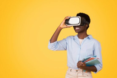African American woman stands against a vibrant yellow background, face obscured by a virtual reality headset, while holding colorful books clipart