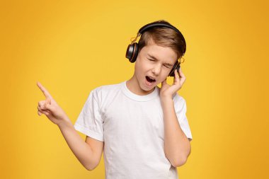 Genç müzik aşığı. Genç çocuk kablosuz kulaklıkla harika bir ses çıkarıyor, boş alanlı turuncu panorama arka planı.