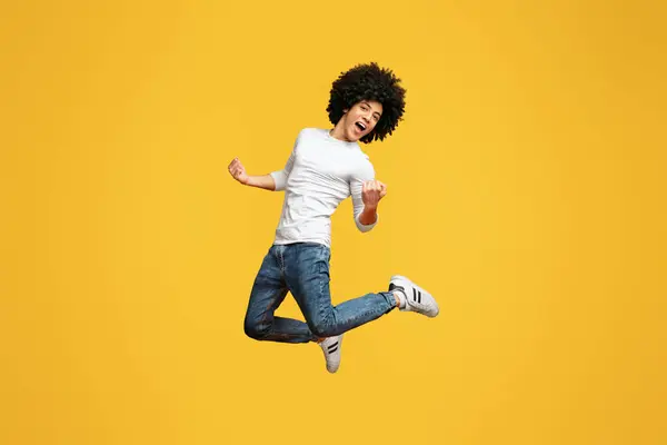 成功を祝います オレンジ色の背景にジャンプ巻き毛の男と幸せな興奮若い千年ブラック ロイヤリティフリーのストック写真