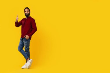 Indian man is standing in front of a bright yellow background, smiling and giving a thumbs up gesture. The man appears confident and happy, with a clear expression of approval, copy space clipart