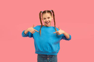 Cheerful young girl with pigtails in a blue sweater confidently pointing at herself against a pink background clipart
