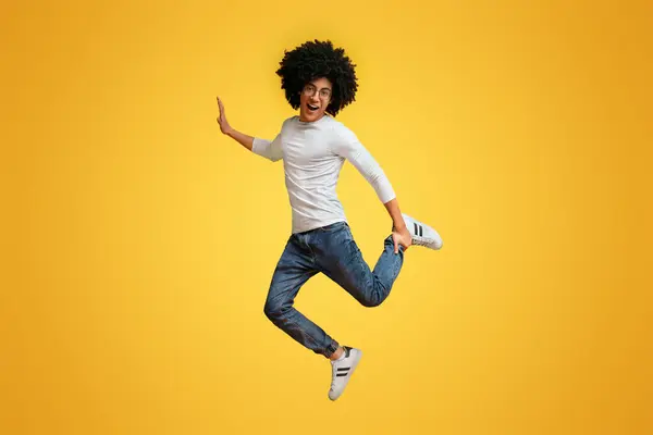 ふさふさしたうれしそうな黒人の男 オレンジ スタジオの背景で片足でジャンプを楽しんで ロイヤリティフリーのストック画像