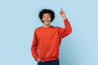 Heyecanlı, kırmızı kazaklı, mavi arka planda izole edilmiş, bir fikri ya da çözümü olan Afro-Amerikan erkeği.