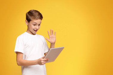 Bir el hareketi yaparken dizüstü bilgisayar tutan genç bir çocuk, muhtemelen heyecan sinyali veriyor ya da bilgi paylaşıyor..