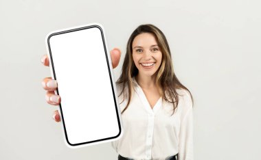Önünde boş bir ekranla cep telefonu tutan bir girişimci kadın. Telefonu yakından inceliyor gibi görünüyor, muhtemelen bildirileri kontrol ediyor ya da bir mesaj yazıyor..