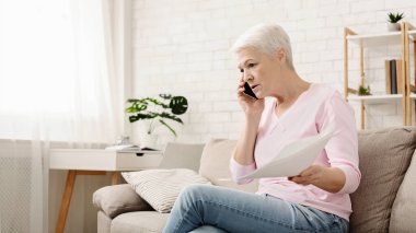 Kızgın yaşlı kadın telefonda konuşurken ve evde çalışan, dizüstü bilgisayar bakarak ve kağıt yazışmasal sallayarak, evde oturan, boş alan