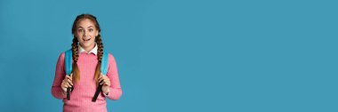 Sırt çantalı, mavi stüdyo arka planında poz veren, fotokopi alanı olan bir genç kız. Eğitim kavramı