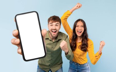 Bir adam ve bir kadın beyaz ekranlı cep telefonunu tutarken görülüyor. Her iki birey de cihazla etkileşime geçerken gülümsüyor, modern iletişim ve teknoloji kullanımını gösteriyor..