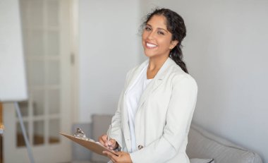 Beyaz takım elbiseli profesyonel bir kadın elinde bir dosya tutuyor. İşine odaklanmış ve meşgul görünüyor..