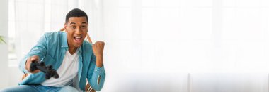 Mavi tişörtlü siyahi adam video oyunu oynuyor ve zaferi kutluyor. İnternet afişi için kopyalama alanı var.