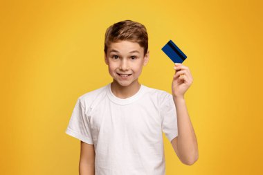 Çocuk bankacılığı. Kredi kartı tutan sevimli çocuk, turuncu stüdyo arka plan