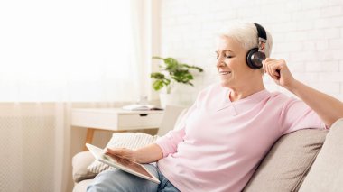 Son sınıf öğrencisi bir kanepede oturmuş, kulaklık takıyor ve müzik dinliyor. Meşgul ve müzik çalmaya odaklanmış görünüyor. Oda rahat ve rahat, yumuşak ışıklandırmalı..