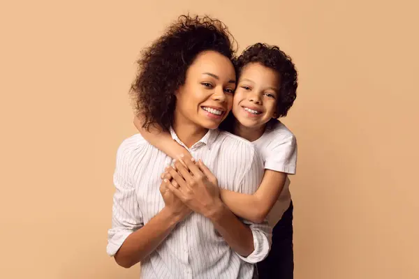 喜ばしいアフリカ系アメリカ人の母親は 両方の白いシャツを着ている柔らかいハグの近くに息子を保持し 親と子供の間の愛情の絆を示しています — ストック写真