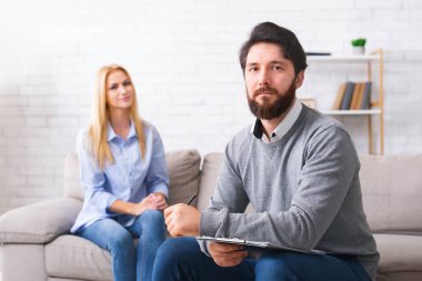 Kendine güvenen psikolog kamera, özel danışmanlık kabinesinde arka planda hasta bakıyor