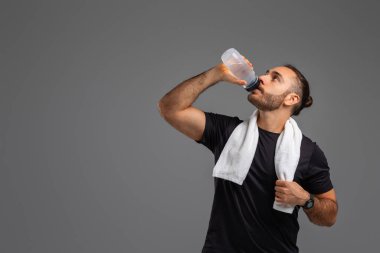 Plastik bir su şişesinden su içen bir adam görülüyor. Şişeyi tek eliyle tutuyor ve ağzına doğru eğiyor, boşluğu kopyalamak için.