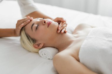 Bu resim, sarışın genç bir kadını lüks bir kaplıcada sakince yüz masajından zevk alırken yakalıyor.