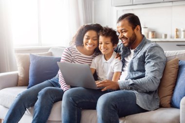 Bir baba, anne ve iki çocuktan oluşan Afro-Amerikan bir aile rahat bir şekilde kanepede oturuyor. Hepsi bir dizüstü bilgisayara odaklanmış, birlikte hareket ediyorlar..