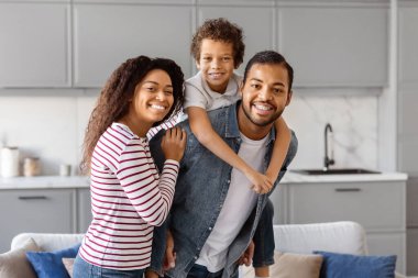 Afro-Amerikalı erkek, kadın ve çocuk aydınlık oturma odasında duruyorlar. Mutlu siyah aile evde birlikte poz veriyor.