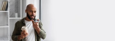 Elinde kahve tutan siyah bir adam ve modern bir ortamda bir telefona sesli notlar alıyor.