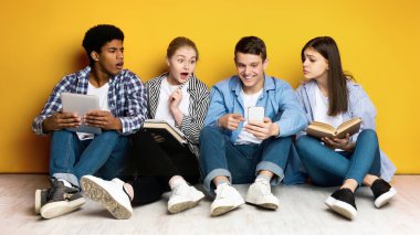 Dört etnik çeşitlilikte genç arkadaştan oluşan bir grup, canlı sarı bir arkaplanda yan yana oturuyorlar. Bir adamın elinde tuttuğu akıllı telefondan etkilenmişler.