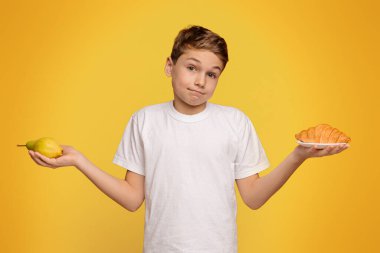 Zor bir karar. Düşünceli genç kruvasan ve taze armut, turuncu stüdyo geçmişi arasında seçim yapıyor.