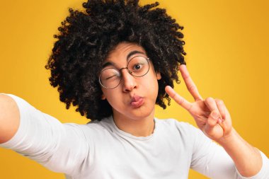 Zamanı kandırmak. Bin yıllık adam komik selfie yapma, barış işareti gesturing, göz kırpma ve dudaklar üfleme, turuncu arka plan