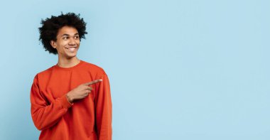 Mutlu Afro-Amerikalı adam yan tarafı gösteriyor ve gülümsüyor, turuncu kazaklı, mavi arka planda soyutlanmış. Seçenekleri ya da yönleri belirlemek için mükemmel, boşluğu kopyala