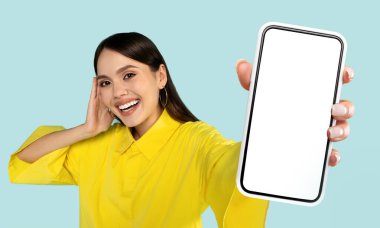 Şok olmuş bir kadın elinde cep telefonuyla beyaz ekranı gösteriyor ve cihazla meşgul gibi görünüyor.