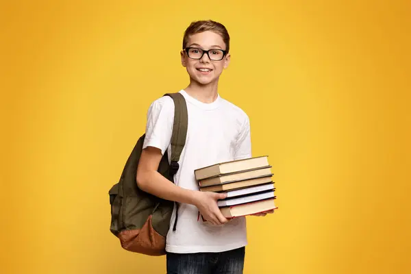 stock image A young boy with short brown hair holding a large stack of colorful books in his arms.