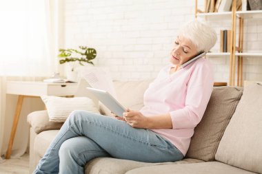 Telefonda meşgul kıdemli kadın danışmanlık istemcisi ve evde dijital tablet üzerinde sözleşme okuma, boş alan