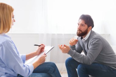 Yakışıklı genç adam kanepede oturan ve psikolog konuşuyor, doktor notlar yapma, boş alan ile panorama