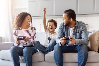 Neşeli bir Afro-Amerikan ailesi oturma odasındaki rahat bir kanepede toplanmış oyun oynuyorlar. Çocuk, heyecan dolu bir bakışla, bir kumandayı tutarken havaya yumruk atıyor.