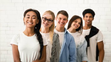 İki kız ve üç erkekten oluşan neşeli bir grup omuz omuza dizilmiş beyaz tuğla bir duvara karşı gelişigüzel poz veriyorlar..