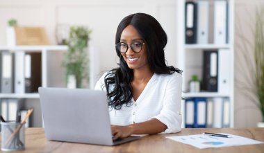 Ofiste dizüstü bilgisayarla çalışan güzel siyahi iş kadını. Afrikalı Amerikalı kadın girişimci daktilo dökümanı, e-postaları kontrol, iş yerindeki çevrimiçi toplantıya katılım