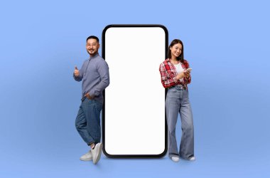 Büyük boy bir telefonun yanında duran Asyalı çift cihaza merakla bakıyor. İnsanlarla karşılaştırıldığında telefon çok büyük görünüyor. Bu da benzersiz bir görsel karşıtlık yaratıyor..