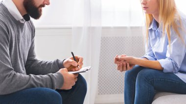 Erkek terapist dikkatle dinler ve not alır. Bu sırada kadın müşteri, iyi aydınlatılmış bir ofis ortamında terapi seansı sırasında endişelerini tartışır..