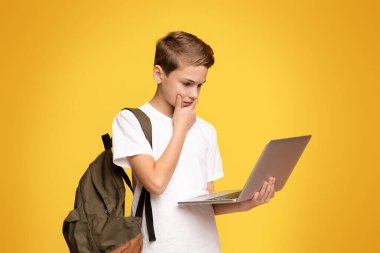 Sırt çantası taşıyan ve dışarıda dizüstü bilgisayarda çalışan genç bir çocuk..