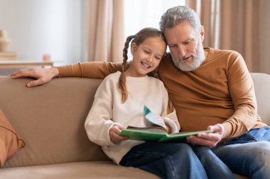 Gülümseyen genç bir kız, bir hikaye anlatma anını paylaşan büyükbabasının yanına oturur. Büyükbaba kitabın kızların elinde olmasına odaklanmış. İkisi de hikayeye sarılmış gibi görünüyor.