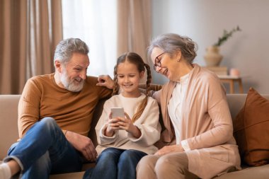 Anne, baba ve çocuktan oluşan bir aile kapalı bir koltukta oturmaktadır. Birbirlerine yakın bir bağ ve ortak ilgi alanlarını gösteren bir cep telefonu ekranına bakıyorlar.