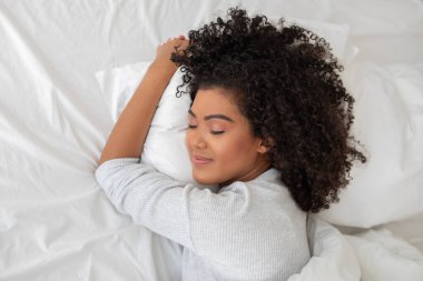 Genç İspanyol kadın yatakta uzanıyor, başını yumuşak bir yastığa koyuyor. Rahat ve rahat görünüyor, belki de uykuya dalmaya hazırdır..