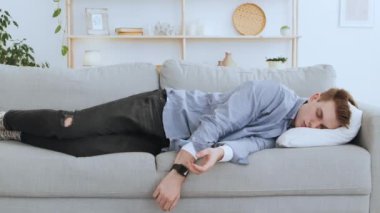 Evdeki kanepede elinde uzaktan kumandayla kestirip duran genç adam, yere düşen TV kumandası.